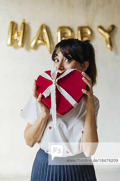 Woman with heart shaped gift box standing in front of wall