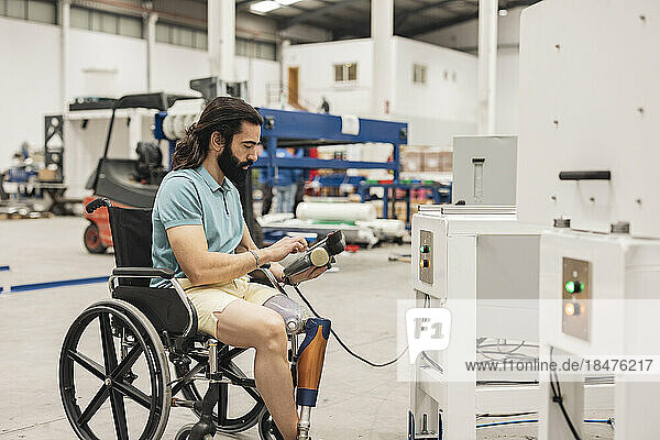 Engineer sitting in wheelchair using controller of machine in industry