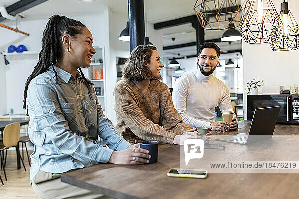 Glückliche Geschäftskollegen sitzen zusammen mit Tassen bei der Kaffeepause im Büro