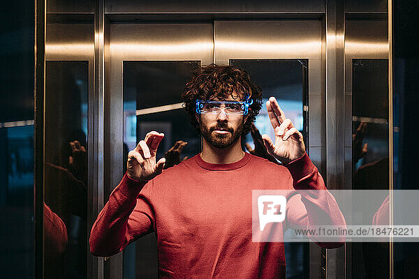 Young man wearing smart eyeglasses gesturing in elevator