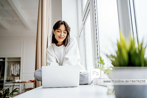 Smiling young woman using laptop at home