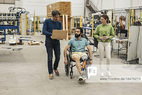 Engineer sitting in wheelchair with colleagues in robotics factory