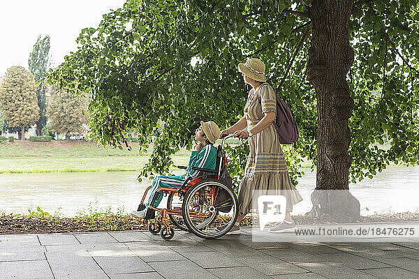 Mother pushing daughter sitting in wheelchair on footpath