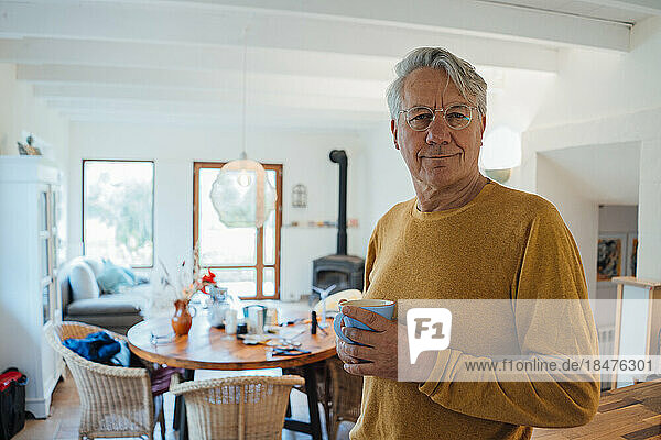 Smiling senior man standing with coffee cup at home