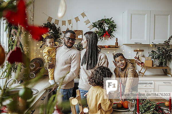 Smiling parents spending time with son and daughters in kitchen at Christmas