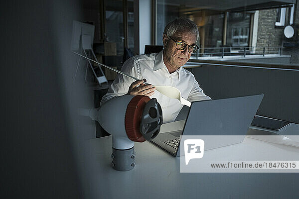 Ingenieur hält Rotorblatt in der Hand und benutzt Laptop im Büro