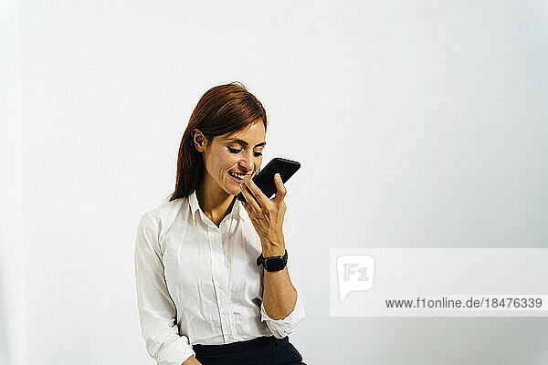 Happy businesswoman talking on smart phone in front of white wall