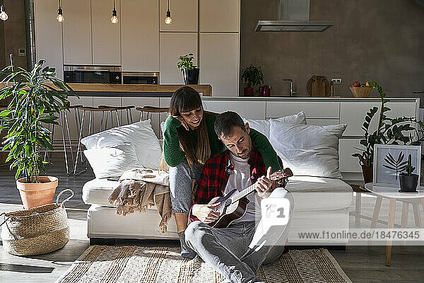 Girlfriend sitting by boyfriend playing guitar at home
