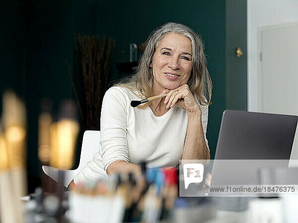 Smiling senior businesswoman with paintbrush sitting in office