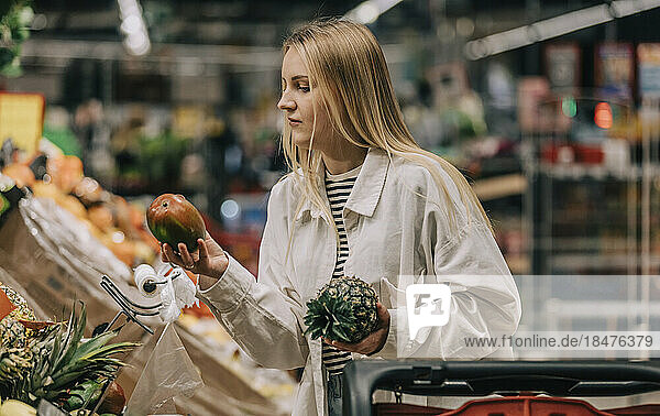 Woman with blond hair examining fruits in supermarket