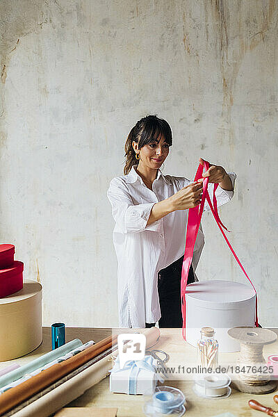 Smiling woman wrapping gift with ribbon