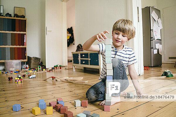 Boy playing with toy blocks sitting on hardwood floor at home