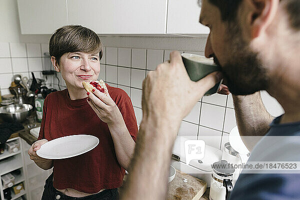 Smiling woman looking at man drinking coffee in kitchen at home
