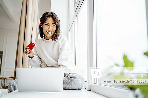smiling young woman shopping with credit card on laptop at home