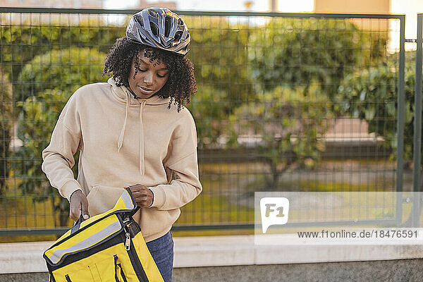Delivery woman with yellow backpack standing in front of fence