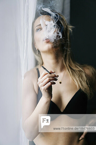 Sensual young woman smoking cigarette at home