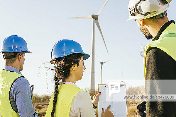 Engineers discussing with technician over wind turbine diagram