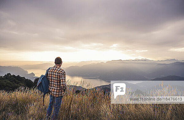 Mature man with backpack standing on mountain at sunset
