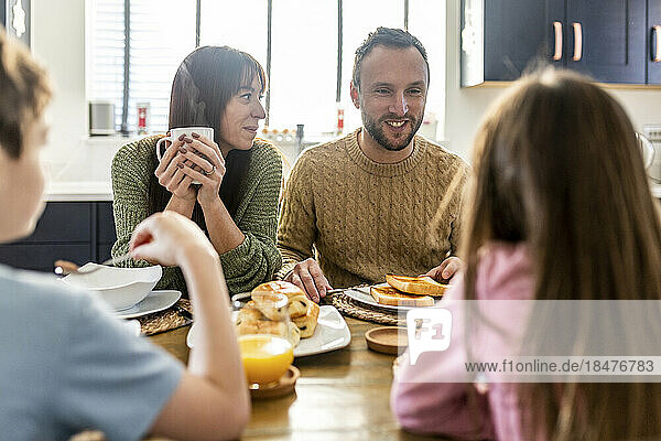 Happy man and woman having breakfast with children at home