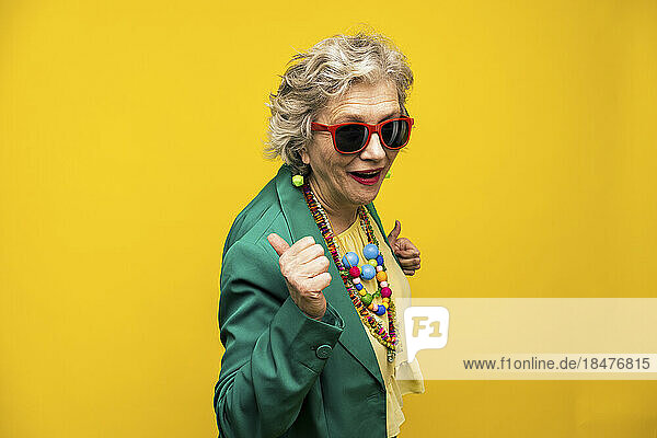Cool senior woman wearing blazer jacket against yellow background