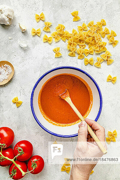 Hand of woman preparing tomato sauce amidst farfalle