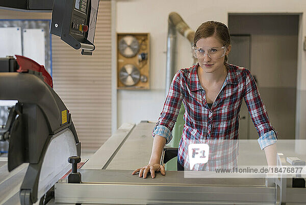 Lächelnde Handwerkerin stützt sich in der Werkstatt auf eine Holzschneidemaschine