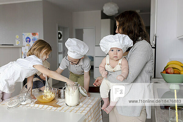 Mutter trägt Jungen mit Kindern und bereitet Teig in der Küche zu