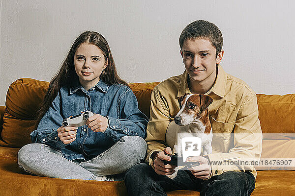 Smiling teenage couple with dog playing video game at home