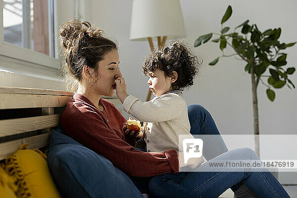 Daughter touching mother's face sitting on sofa