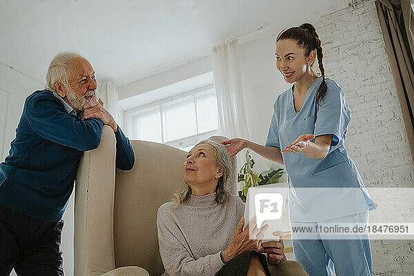 Happy nurse gesturing by senior patients at home