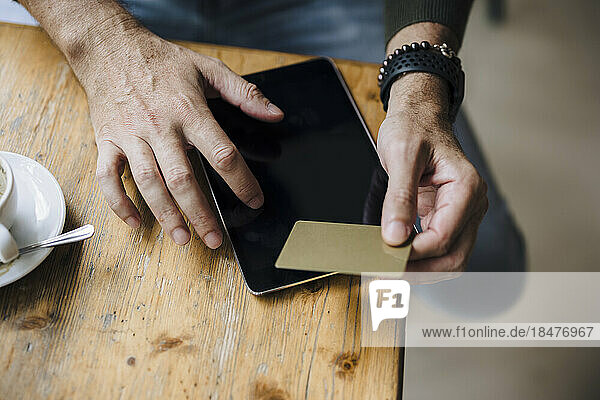 Man holding credit card using tablet PC on table in cafe