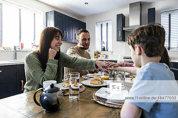 Glückliche Familie genießt gemeinsam das Frühstück mit gestapelten Händen am Tisch