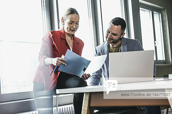 Businesswoman reading document with colleague at workplace