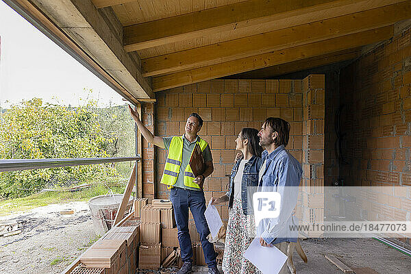 Glücklicher Bauunternehmer  der mit einem älteren Paar auf der Baustelle diskutiert