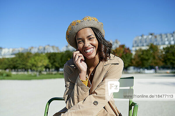 Happy young woman wearing beret sitting on chair in front of blue sky