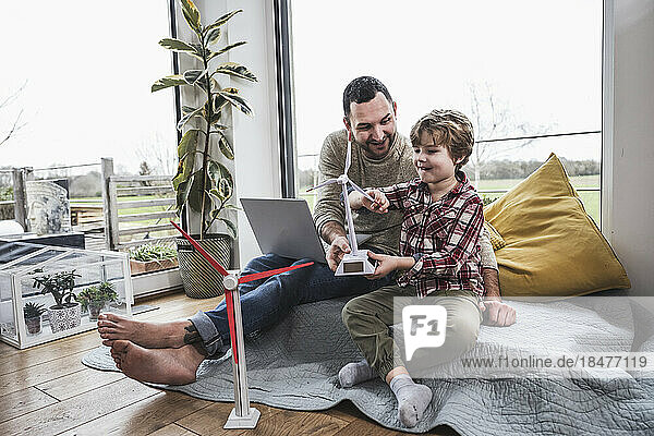 Father and son playing with wind turbine model sitting at home