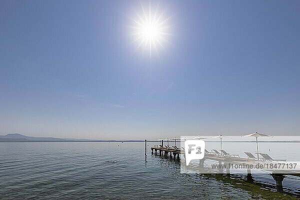 Italy  Veneto  Bardolino  Sun shining over deck chairs and umbrellas on lakeshore jetty