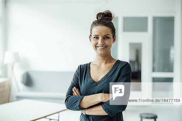 Happy businesswoman standing with arms crossed in home
