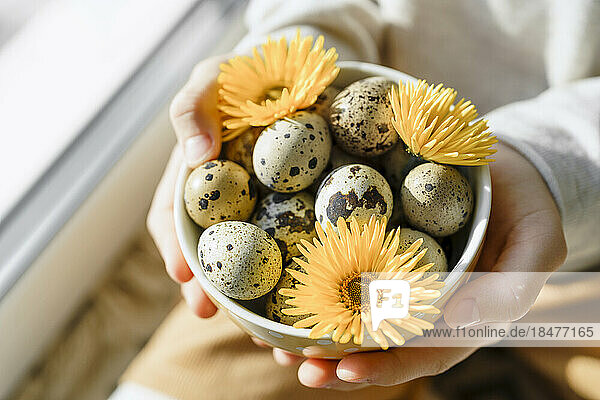 Hands of girl holding Easter egg with sunflowers in bowl at home