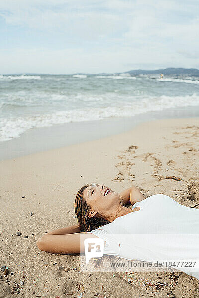 Woman with hands behind head lying on sand by sea at beach