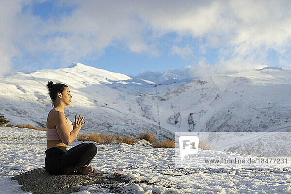 Frau in Gebetsposition macht Yoga auf schneebedecktem Berg
