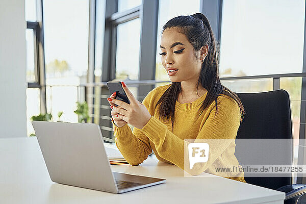 Junge Geschäftsfrau nutzt Mobiltelefon per Laptop im Büro