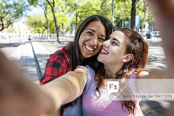 Happy lesbian couple taking selfie on footpath