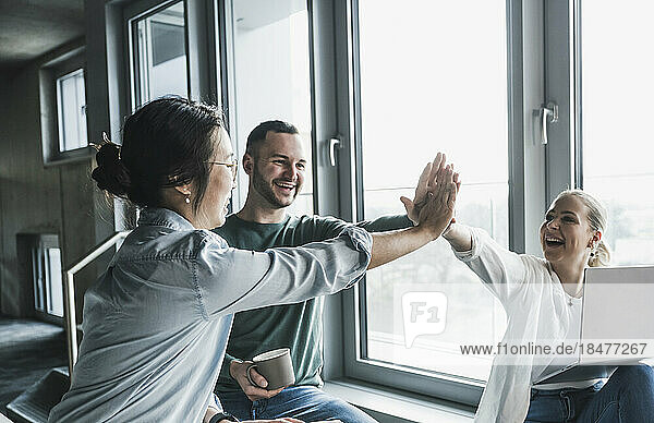 Happy business colleagues giving high-five to each other at office