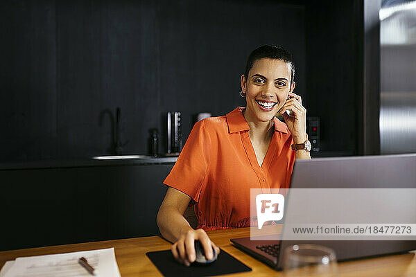 Happy freelancer with short hair sitting in front of laptop at table