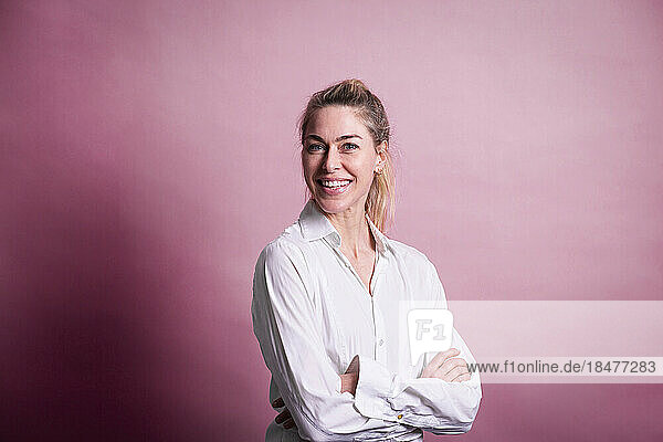 Happy businesswoman standing with arms crossed against colored background