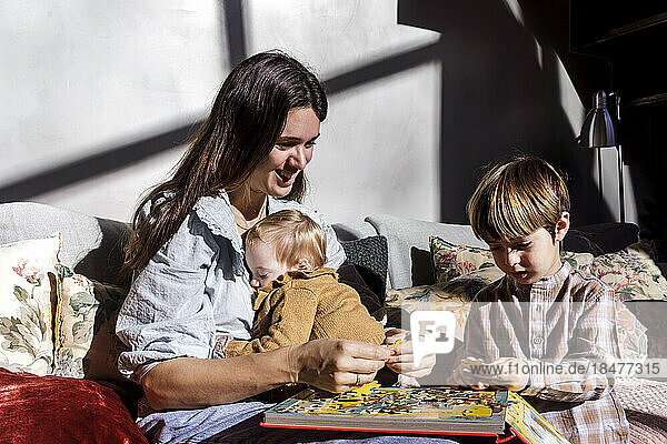 Smiling mother solving jigsaw puzzle with children at home