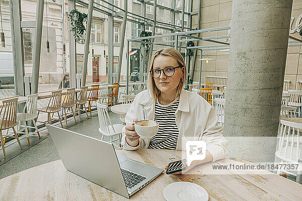 Businesswoman wearing eyeglasses holding coffee cup sitting at cafe