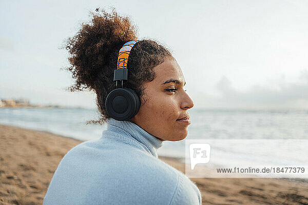 Nachdenkliche junge Frau mit Kopfhörern  die am Strand Musik hört