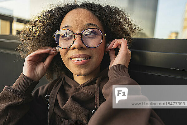 Young woman with curly hair wearing wireless in-ear headphones
